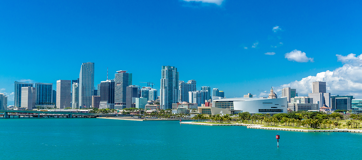 This is a photo from Shutterstock. It is the Miami skyline. This area of Miami represents the Brickell and Downtown neighborhoods. The picture was taken off of the bay. There are skyscrapers, the famous concert arena, and the blue ocean water which Miami is famous for.